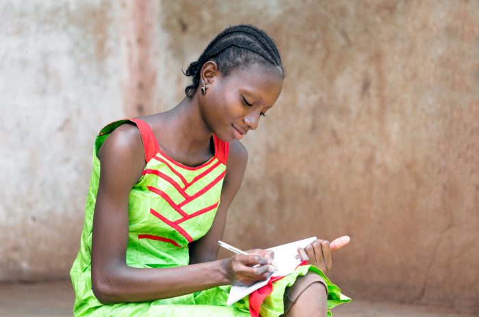 Gorgeous Black African Girl writing and drawing on her exercise book in a school using a pen. By buying this photo you help and support our social projects in Mali. Young schoolgirl education symbol.
